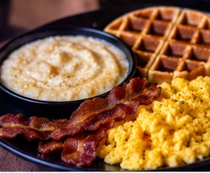 Illustrative breakfast plate with waffles, eggs, bacon and grits